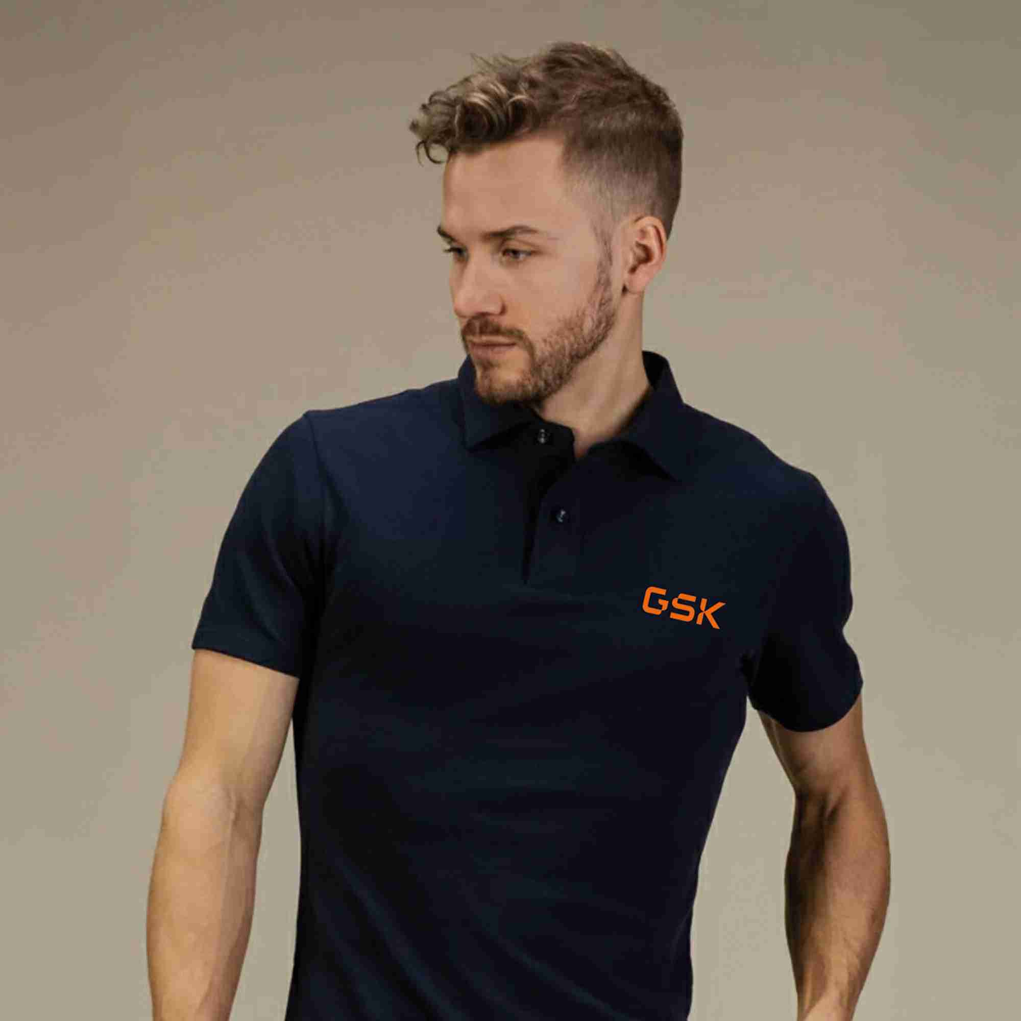 Man wearing a navy blue polo shirt with an orange GSK logo on the left chest area.