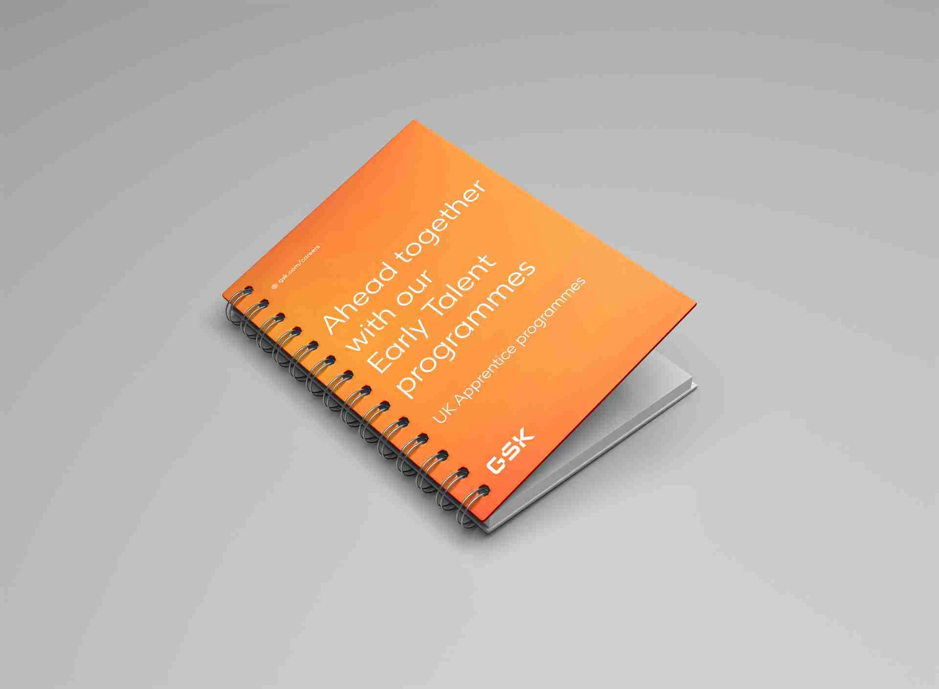 Spiral-bound notebook with an orange cover featuring text about GSK's Early Talent programmes.