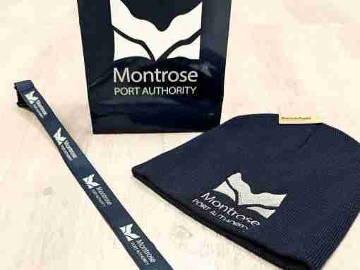 Montrose Port Authority Merchandise Set Montrose Port Authority branded beanie, lanyard, and bag displayed together on a flat surface.